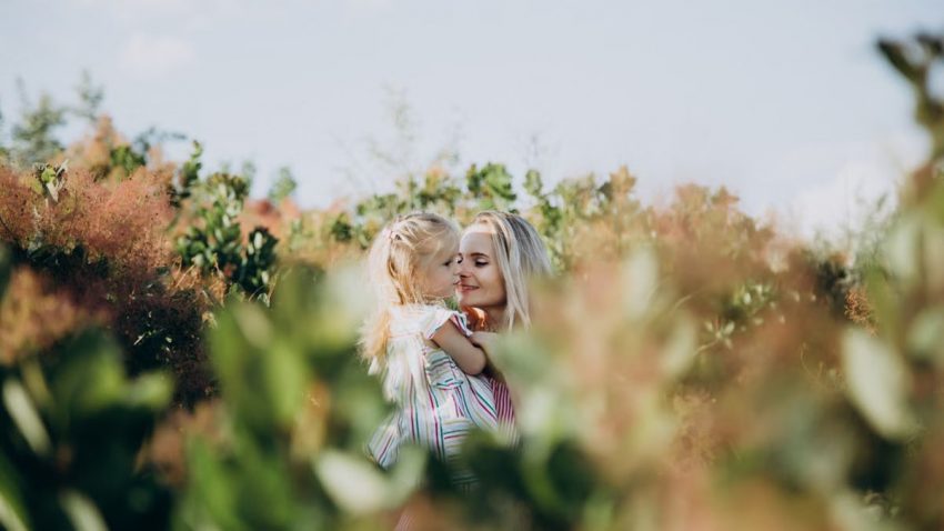 A touching moment between a mother and daughter surrounded by lush greenery outdoors.